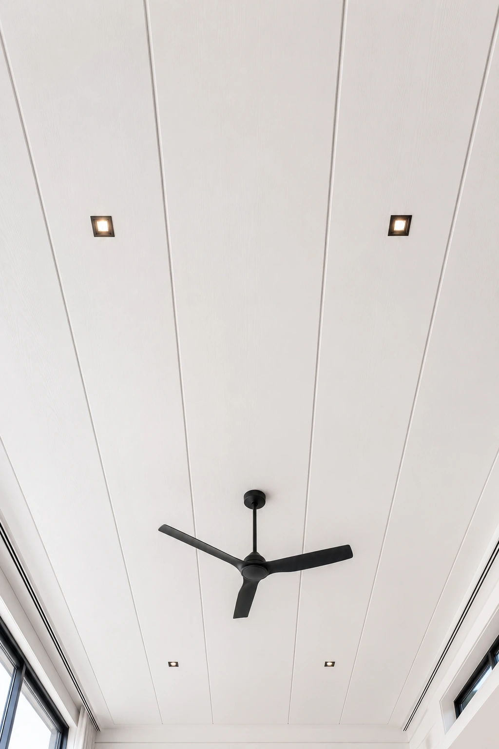 Minimal white vertical shiplap ceiling with sleek black ceiling fan, recessed square lighting, clean contemporary architecture, smooth painted ceiling panels, bright modern interior, minimalist ceiling inspiration, elegant white wood ceiling design, timeless modern shiplap ceiling ideas for open spaces