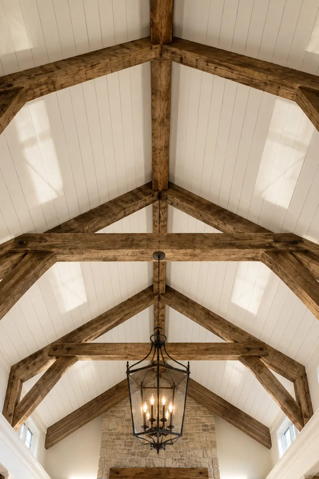Vaulted white shiplap ceiling with exposed rustic reclaimed wood beams, dramatic timber trusses, oversized black lantern chandelier, soaring cathedral ceiling, rustic luxury architecture, warm natural wood textures, timeless farmhouse ceiling inspiration, elegant high ceiling design, statement beam ceiling with white wood planks, custom shiplap ceiling ideas for grand living spaces