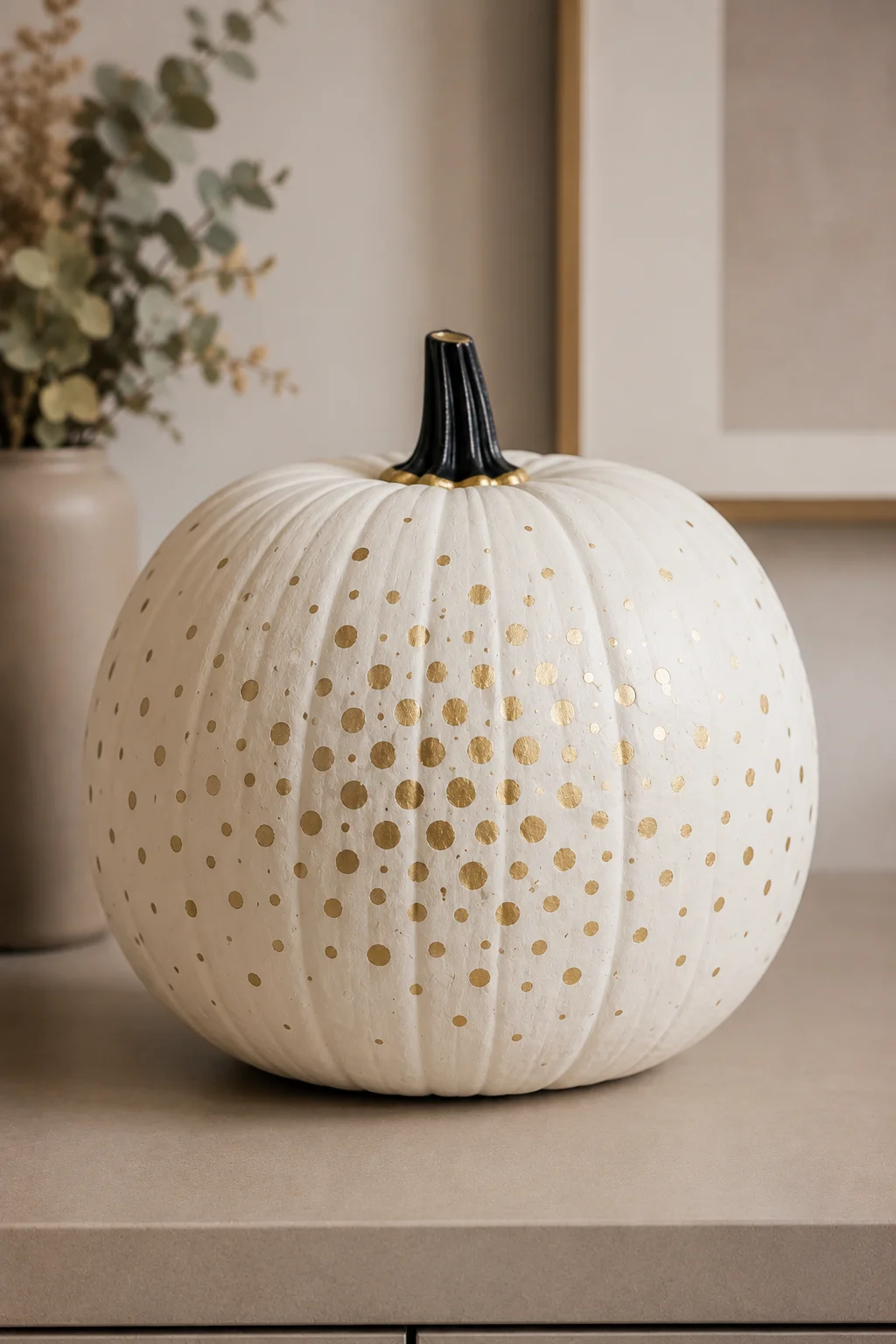 A large warm white pumpkin decorated with delicate champagne gold dots in varied sizes, creating a refined scattered pattern with a black stem and minimalist styling for modern fall decorating.